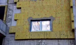 Pannelli isolanti gialli fissati con tasselli rossi su un edificio in costruzione. Si notano alcuni difetti cappotto termico, come fughe e irregolarità.
