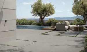 Elegante pavimentazione esterna in gres porcellanato grigio, che circonda una piscina e un'area relax con divani e tavolino in legno.