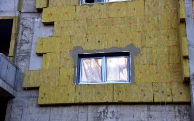 Pannelli isolanti gialli fissati con tasselli rossi su un edificio in costruzione. Si notano alcuni difetti cappotto termico, come fughe e irregolarità.