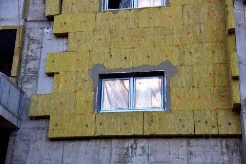Pannelli isolanti gialli fissati con tasselli rossi su un edificio in costruzione. Si notano alcuni difetti cappotto termico, come fughe e irregolarità.