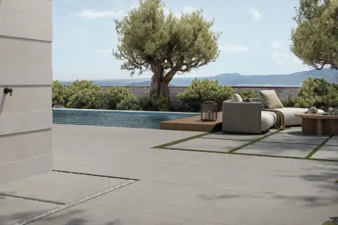 Elegante pavimentazione esterna in gres porcellanato grigio, che circonda una piscina e un'area relax con divani e tavolino in legno.
