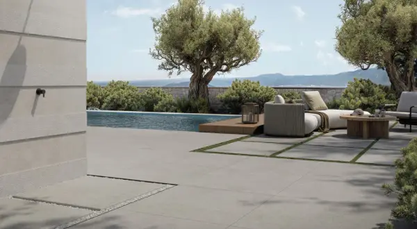 Elegante pavimentazione esterna in gres porcellanato grigio, che circonda una piscina e un'area relax con divani e tavolino in legno.