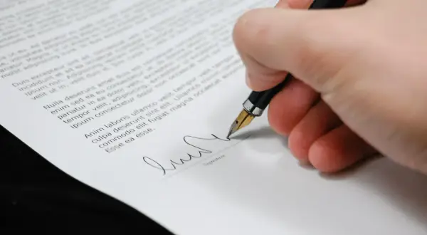 Firma su un documento, con una penna stilografica che scrive. Il peritale significato di un accordo si concretizza in questo gesto.