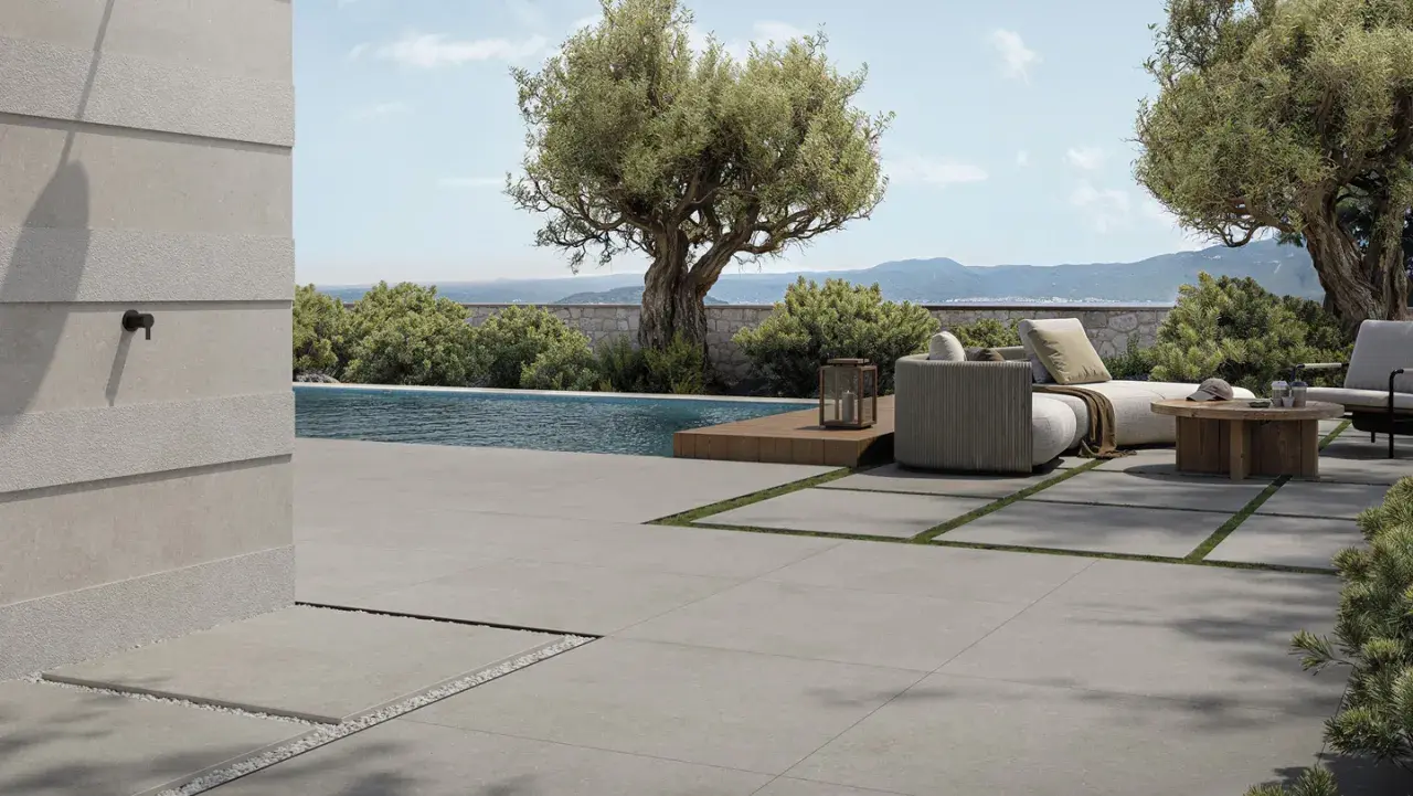 Elegante pavimentazione esterna in gres porcellanato grigio, che circonda una piscina e un'area relax con divani e tavolino in legno.