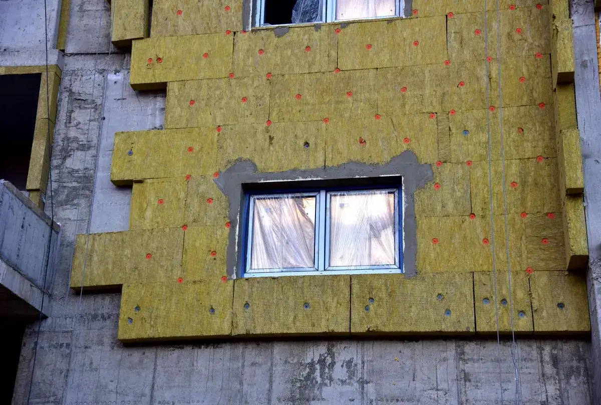 Pannelli isolanti gialli fissati con tasselli rossi su un edificio in costruzione. Si notano alcuni difetti cappotto termico, come fughe e irregolarità.