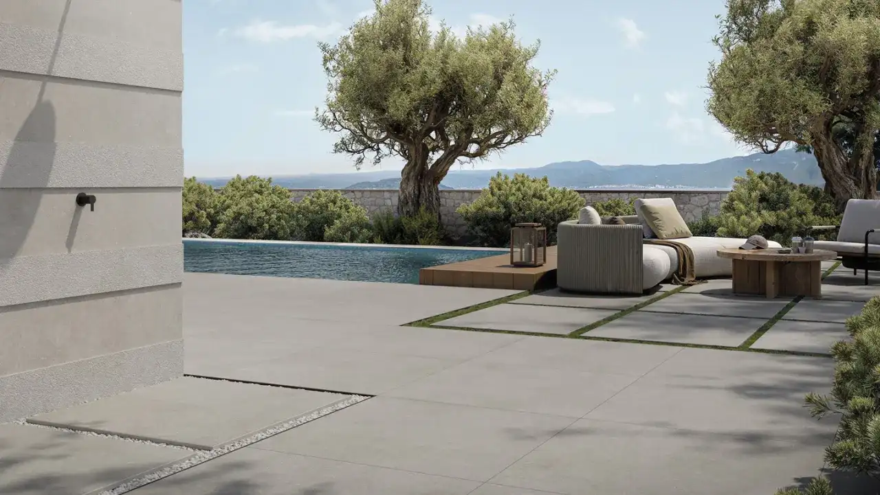 Elegante pavimentazione esterna in gres porcellanato grigio, che circonda una piscina e un'area relax con divani e tavolino in legno.