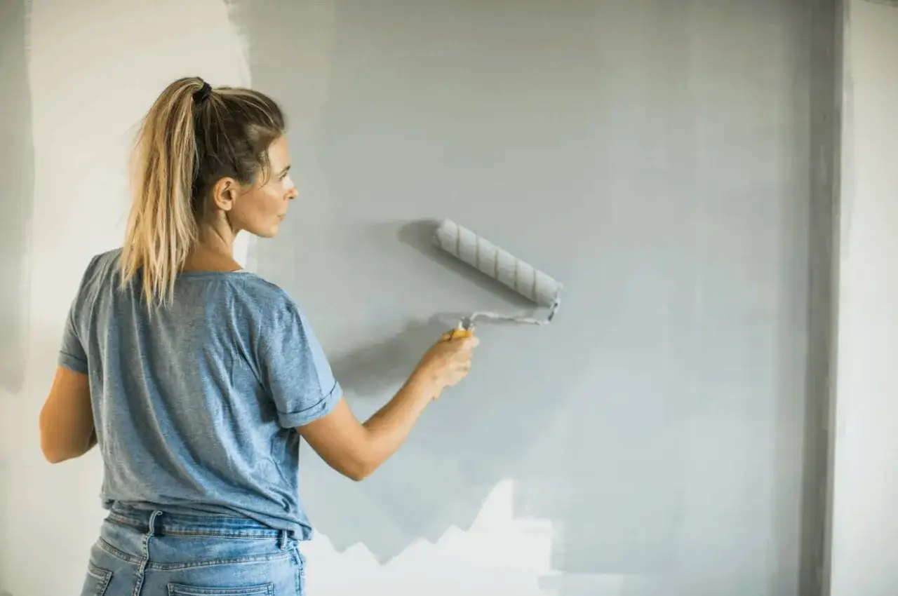 Donna dipinge un muro con vernice acrilica, trasformando la stanza. La vernice acrilica a cosa serve? A dare nuova vita agli spazi!