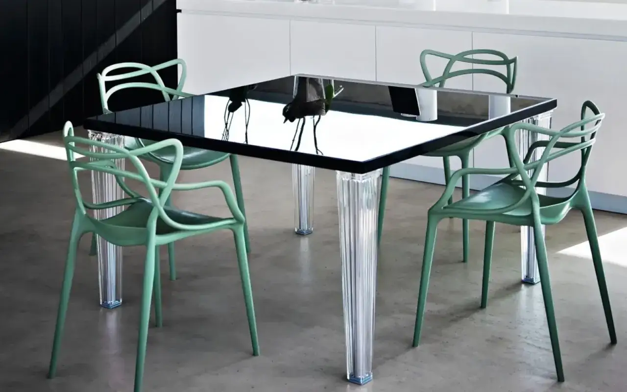 A modern black glass table with clear fluted legs is surrounded by four mint green Kartell chairs.