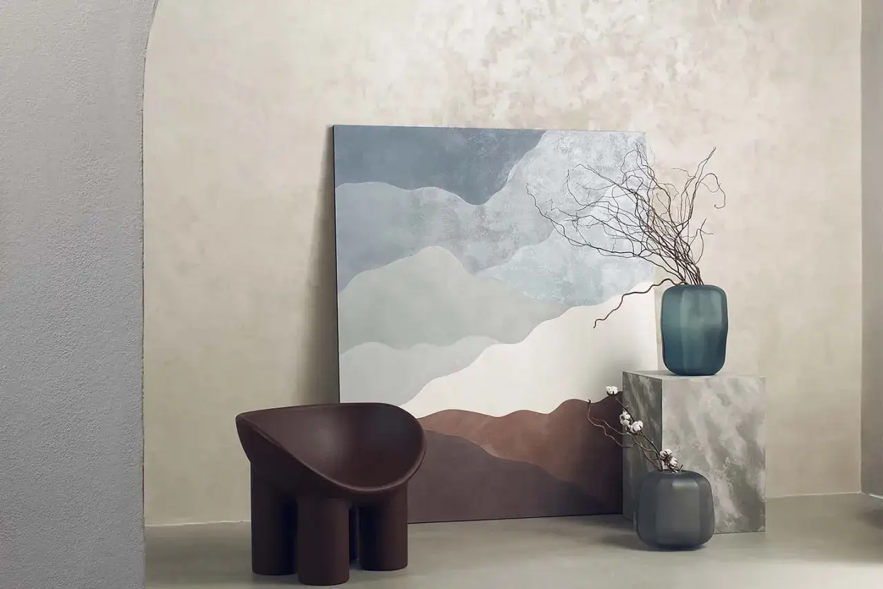 Un soggiorno moderno con un quadro astratto che evoca paesaggi montani, una poltrona scultorea e vasi decorativi. I stili di pittura per interni si fondono con arredi di design.