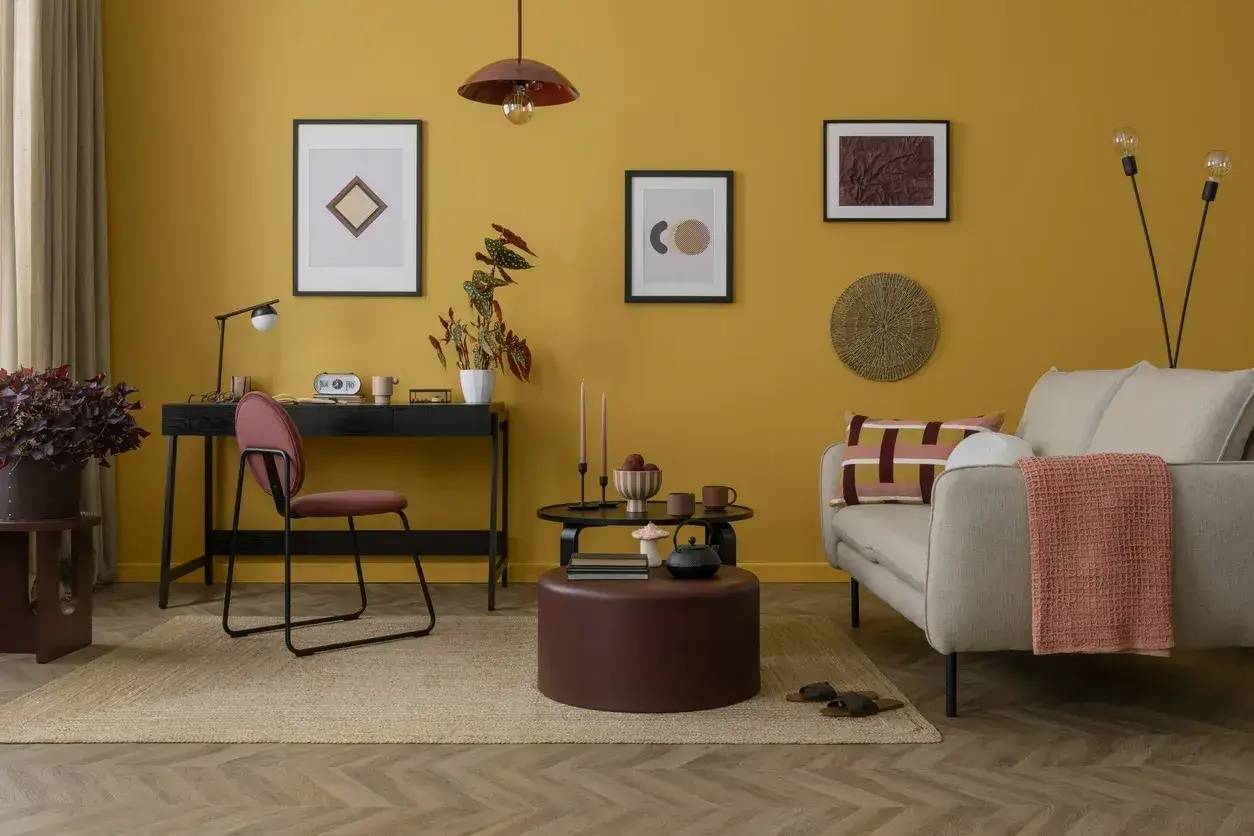 Un soggiorno con pareti color ocra e abbinamenti caldi. Un divano beige, cuscini geometrici e una coperta corallo creano un'atmosfera accogliente.