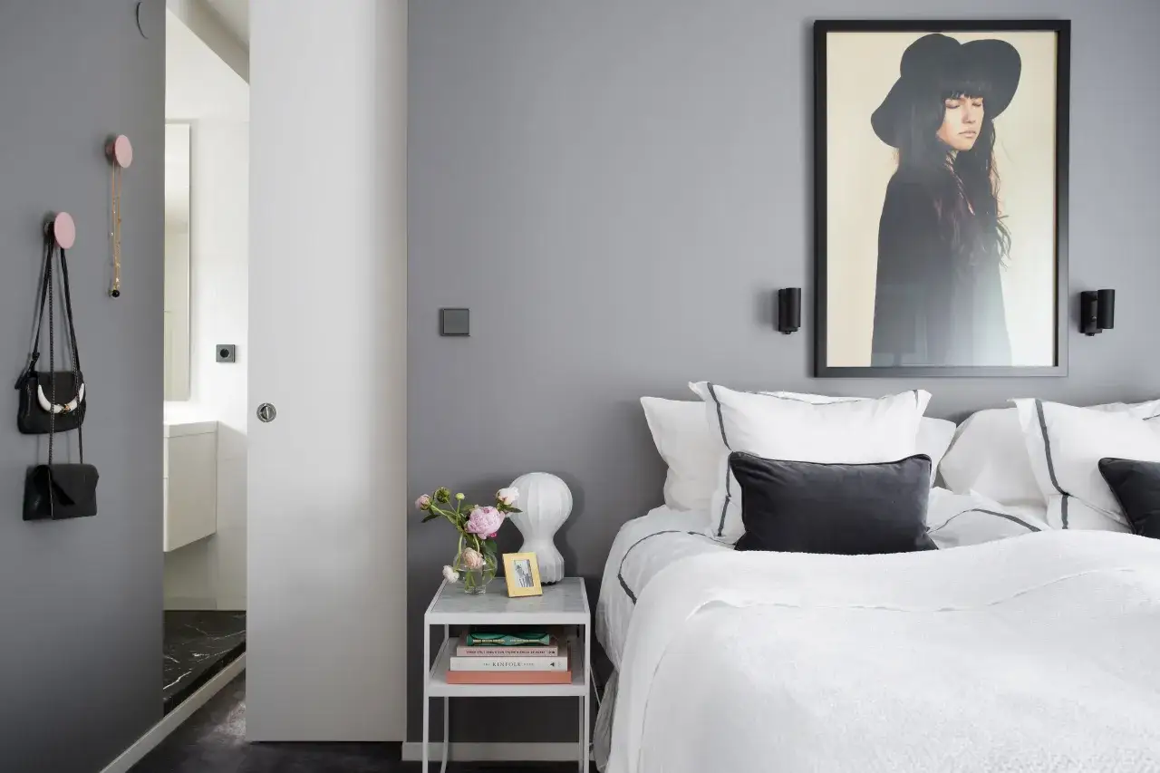 Camera da letto minimalista con letto bianco, quadro di una donna con cappello, e accessori che creano illusioni ottiche trucchi per allargare una stanza.