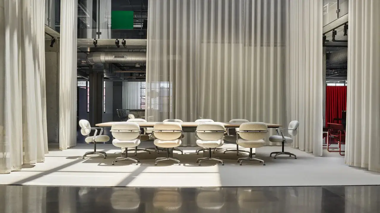 Sala riunioni moderna con tavolo e sedie, separata da tende leggere. Il passaggio minimo tra mobili garantisce fluidità.