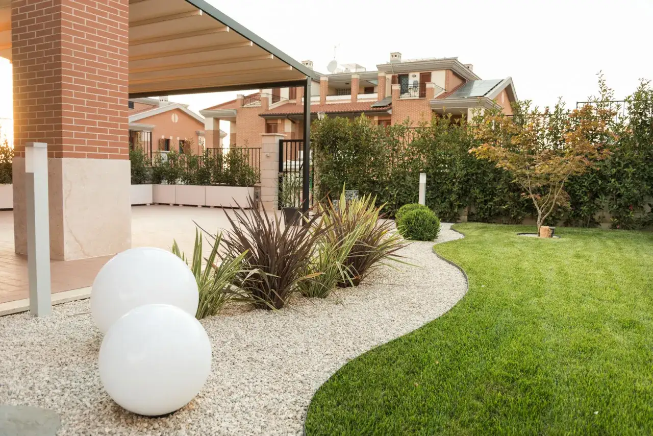Un moderno giardino progetto con sfere luminose, ghiaia bianca, prato curato e siepi verdi.