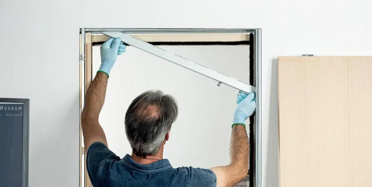 Installazione controtelaio porta scorrevole in cartongesso: un operaio con guanti azzurri fissa un profilo metallico.