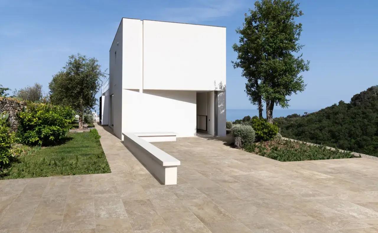 Modern white house with a bench and a patio featuring a durable rivestimento in cemento per esterni that blends with the natural landscape.