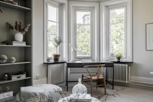 Scrivania con vista finestra, un angolo studio luminoso con sedia in legno e piante.