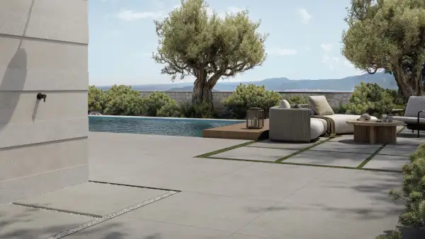 Elegante pavimentazione esterna in gres porcellanato grigio, che circonda una piscina e un'area relax con divani e tavolino in legno.